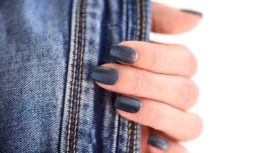 Beyaz arka plan üzerinde kot ile el ile koyu mavi manikürlü tırnaklar.