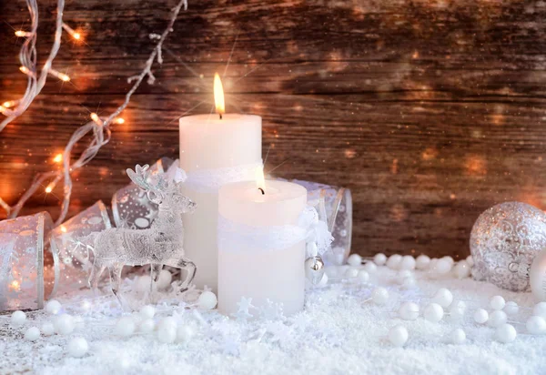 Δύο κεριά καύση με ένα ελάφι με Χριστουγεννιάτικες διακοσμητικές μπάλες στο χιόνι και φώτα των Χριστουγέννων. — Φωτογραφία Αρχείου