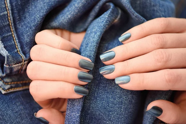 Mãos com unhas de manicure azul escuro sobre fundo têxtil jeans — Fotografia de Stock