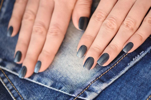 Mãos com unhas de manicure azul escuro sobre fundo têxtil jeans — Fotografia de Stock