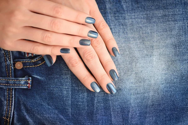 Mãos com unhas de manicure azul escuro sobre fundo têxtil jeans — Fotografia de Stock