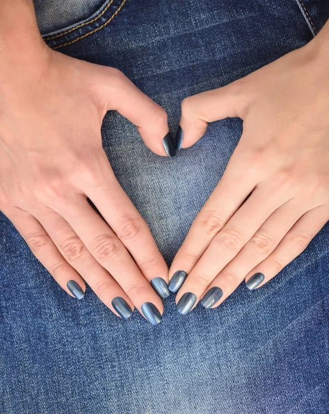 Hand in de vorm van hart voor liefde tegen jeans textiel achtergrond. Handen met donker blauwe gemanicuurde nagels — Stockfoto