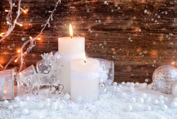 Dos velas encendidas con un ciervo con bolas decorativas de Navidad en la nieve y las luces de Navidad . — Foto de Stock