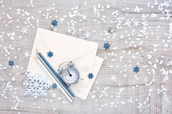 目覚まし時計、鉛筆、おめでとう、雪と光の木製の背景に紙吹雪の封筒 — ストック写真
