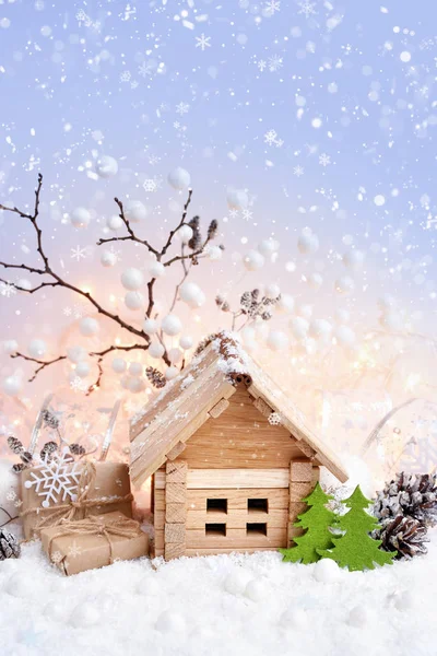 Paesaggio decorativo natalizio con casetta in neve, regali e decorazioni su sfondo di luci natalizie — Foto Stock