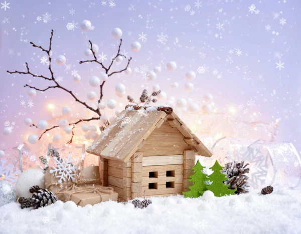 Рождественский декоративный пейзаж с игрушечным домиком в снегу, подарками и украшениями на фоне рождественских огней — стоковое фото