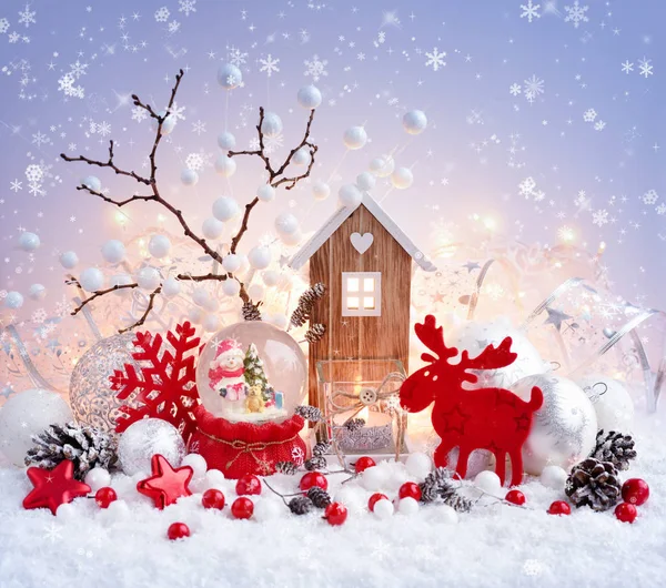 Una bola de nieve con muñeco de nieve con decoraciones de Navidad y casa de juguete en la nieve y las luces de Navidad —  Fotos de Stock