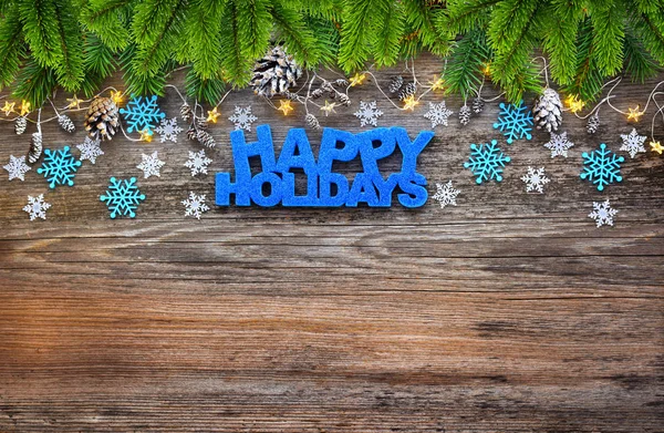 Hälsning ”Happy Holidays”, snöflinga, julbelysning och spruce grenar på ett träbord. — Stockfoto