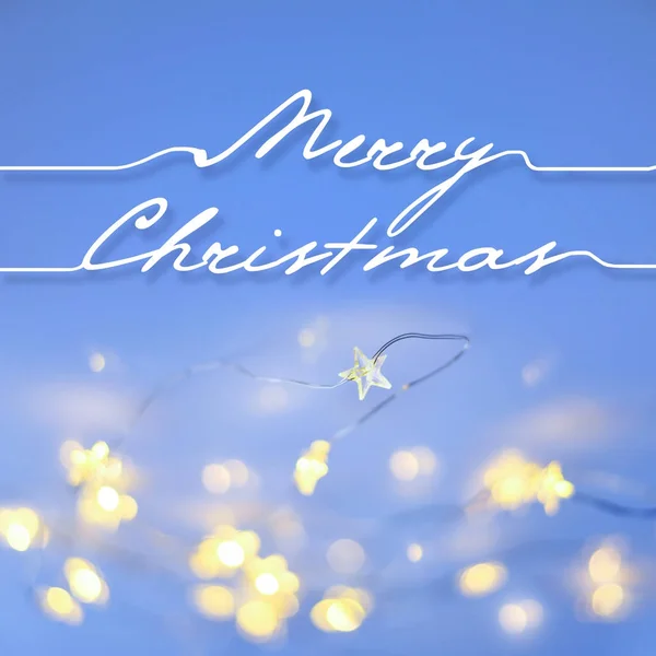 ขอแสดงความยินดี "สุขสันต์วันคริสต์มาส" บนพื้นหลังสีฟ้าด้วยแสงคริสต์มาส . — ภาพถ่ายสต็อก