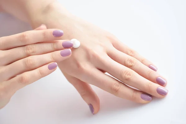 Las manos femeninas con la manicura rosada que aplica la crema. El concepto de cuidado de la piel . — Foto de Stock