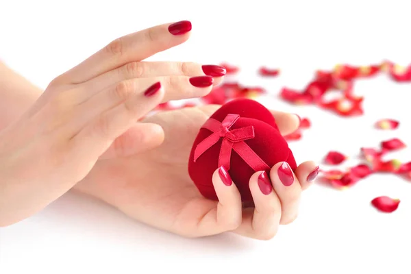 Hermosas manos femeninas con manicura roja sosteniendo una caja de forma de corazón . — Foto de Stock