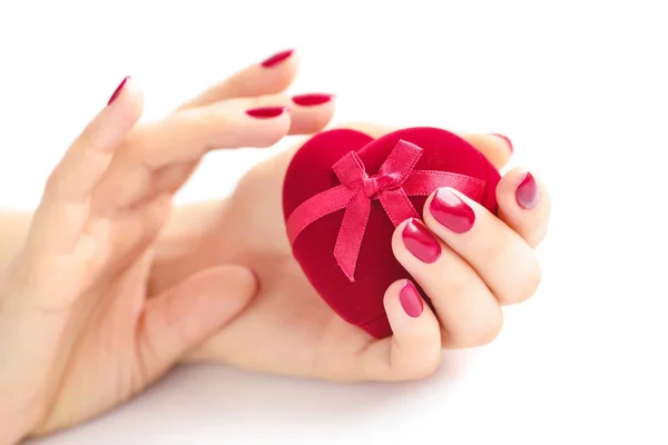 Belas mãos femininas com manicure vermelho segurando uma caixa de em forma de coração — Fotografia de Stock
