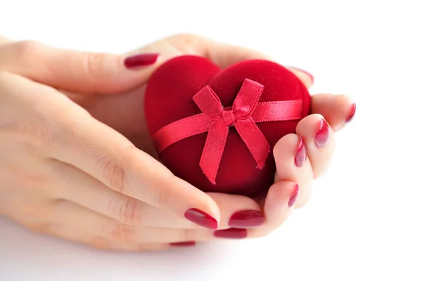 Hermosas manos femeninas con manicura roja sosteniendo una caja de forma de corazón —  Fotos de Stock