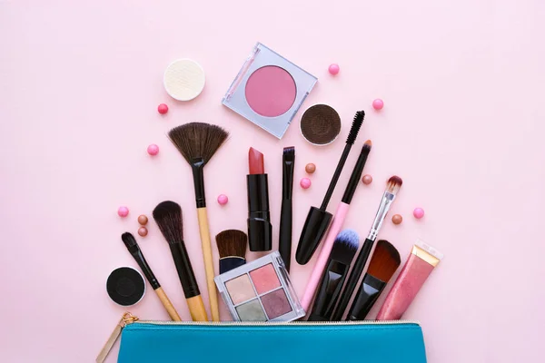 Una bolsa de cosméticos azul con productos de maquillaje que se derraman sobre un fondo rosa pastel —  Fotos de Stock