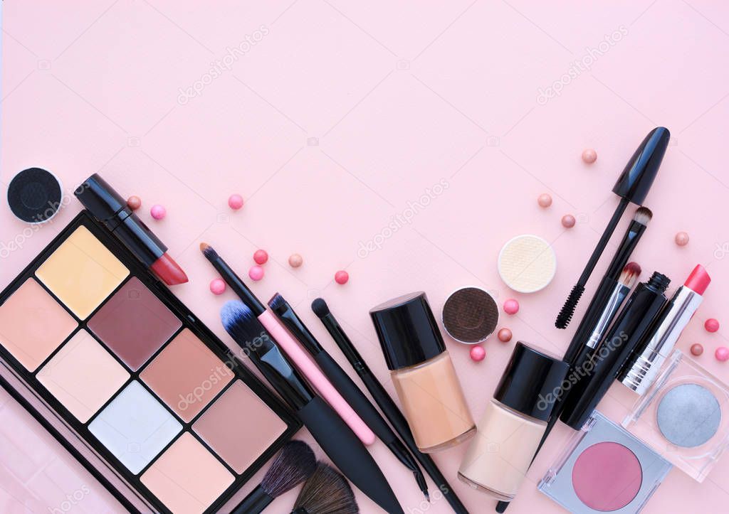 Makeup brush and decorative cosmetics on a pastel pink background with empty space.