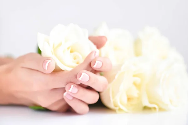 Händerna på en kvinna med vacker fransk manikyr och vita rosor — Stockfoto