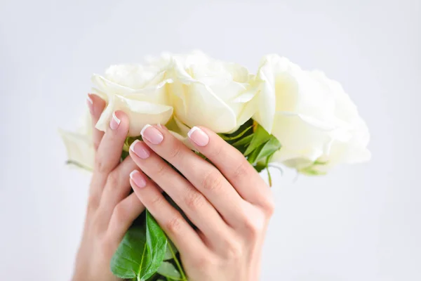 Manos de una mujer con hermosa manicura francesa y ramo de rosas blancas — Foto de Stock
