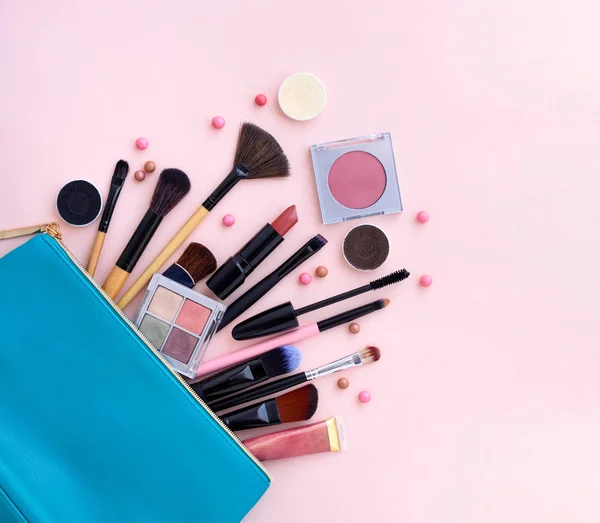 Pastel pembe bir arka plan üzerine dışarı dökülmesini makyaj ürünleri ile mavi kozmetik çantası — Stok fotoğraf