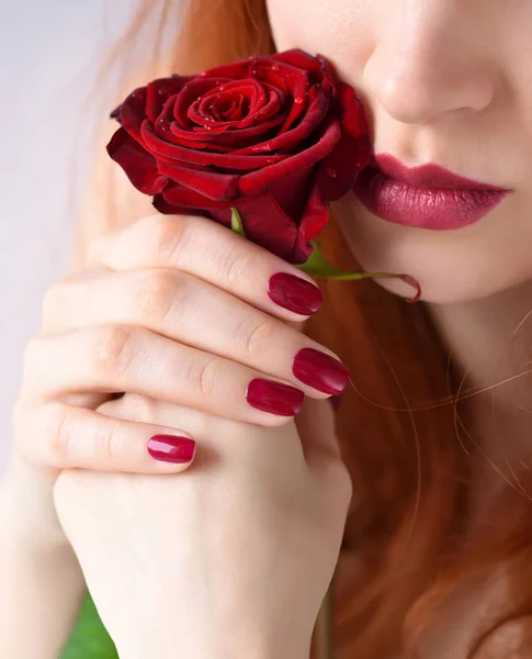 Arckép piros rózsa virág. Vörös ajkak és a körmök. Gyönyörű vörös hajú fiatal nő. — Stock Fotó
