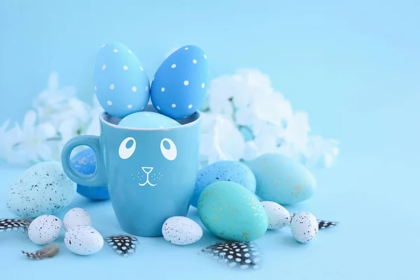 Ovos de Páscoa e uma xícara na forma de um coelho em um fundo azul — Fotografia de Stock