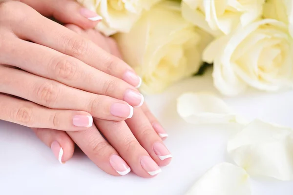 Ręce kobiety z pięknym francuskim manicure i białe róże — Zdjęcie stockowe