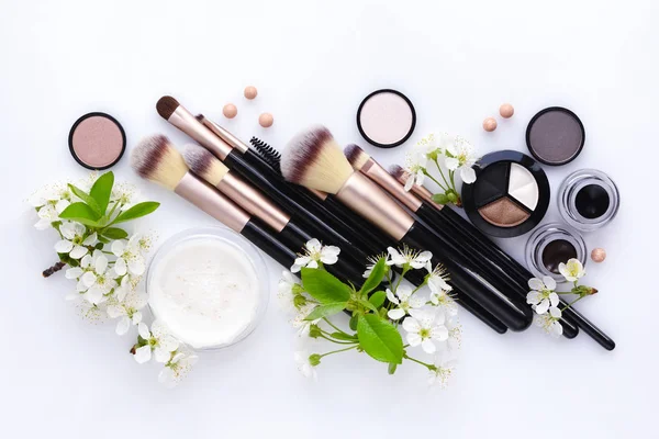 Cepillo de maquillaje y cosméticos decorativos con rama en flor sobre fondo blanco — Foto de Stock