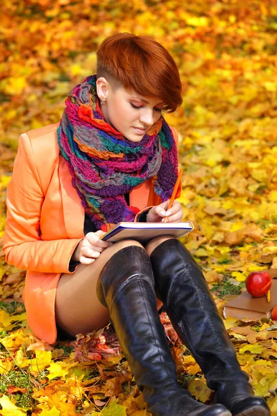 Chica estudiante pelirroja con cuaderno sobre un fondo hojas de otoño — Foto de Stock