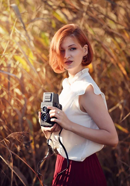 Hermosa joven pelirroja mujer sostiene una cámara retro — Foto de Stock
