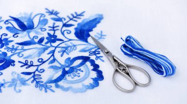 Nakış, iplik ve makas. Beyaz çiçekli mavi süs.