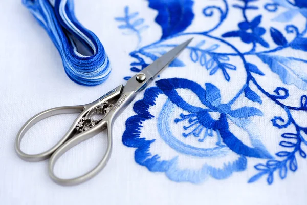 Výšivky, nitě a nůžky. Modrá květinová ozdoba na bílém pozadí — Stock fotografie