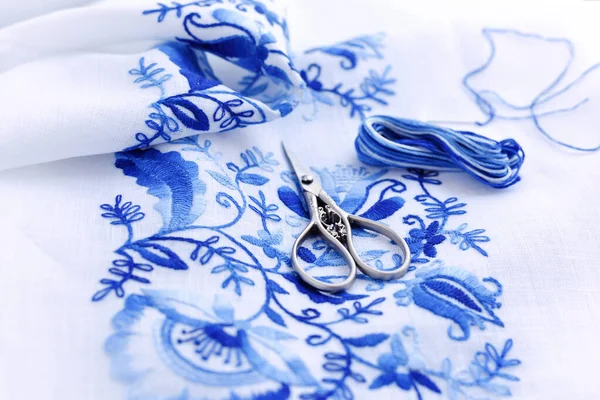 Výšivky, nitě a nůžky. Modrá květinová ozdoba na bílém — Stock fotografie