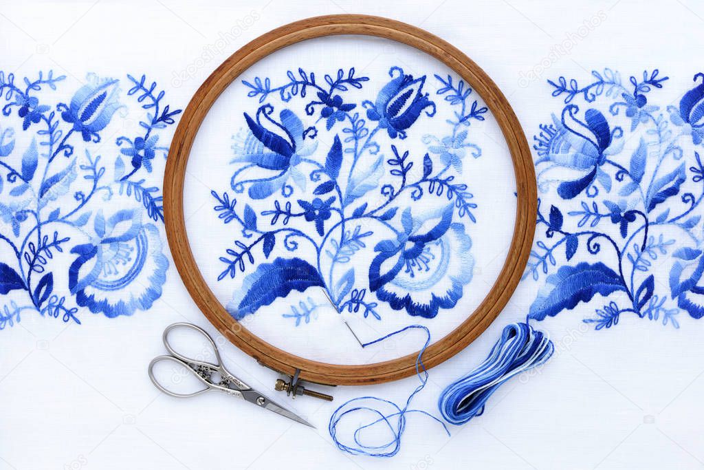 Embroidery hoop with fabric, sewing needle and thread, top view.