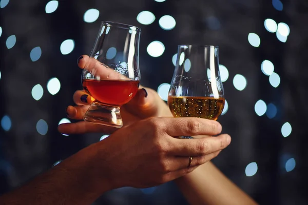 A couple makes a toast with two glasses of whiskey on festive background — Stock Photo, Image