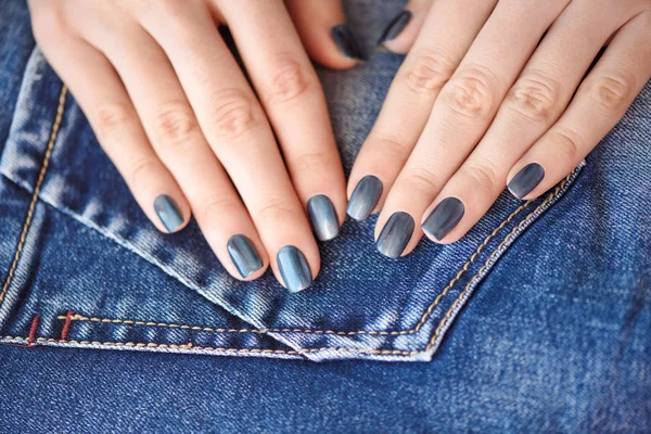 Mãos com unhas de manicure azul escuro sobre fundo têxtil jeans — Fotografia de Stock