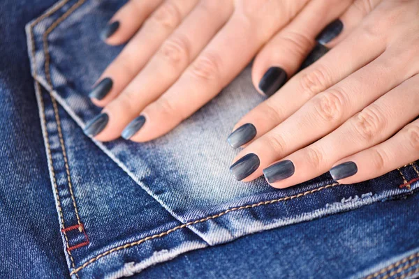 Hands with dark blue manicured nails on jeans textile background