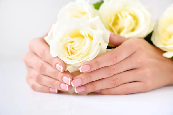 Händerna på en kvinna med vacker fransk manikyr och vita rosor — Stockfoto