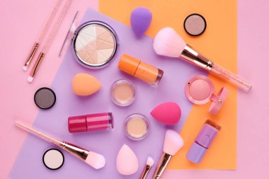 Makyaj fırçaları ve renkli arka planda dekoratif kozmetik ürünler. Üst görünüm