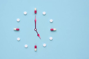 Pastel mavi arka plandaki haplardan ve kapsüllerden yapılmış bir saat. İlaç kullanmak için doğru zaman. Düz yatıyordu.