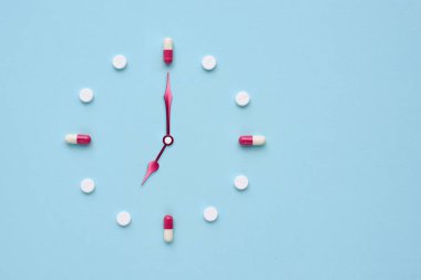 Pastel mavi arka plandaki haplardan ve kapsüllerden yapılmış bir saat. İlaç kullanmak için doğru zaman. Düz yatıyordu.