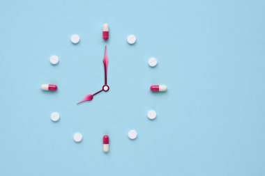 Pastel mavi arka plandaki haplardan ve kapsüllerden yapılmış bir saat. İlaç kullanmak için doğru zaman. Düz yatıyordu.