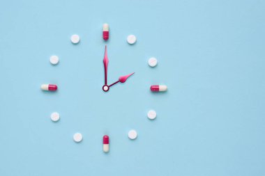 Pastel mavi arka plandaki haplardan ve kapsüllerden yapılmış bir saat. İlaç kullanmak için doğru zaman. Düz yatıyordu.