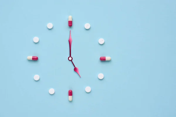 时钟是用药丸和胶囊在淡蓝色背景下制成的 正确的时间使用药物 平躺在床上 — 图库照片