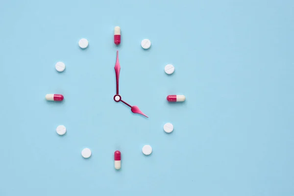Clock created from pills and capsules on pastel blue background. Right time for using medicines. Flat lay.