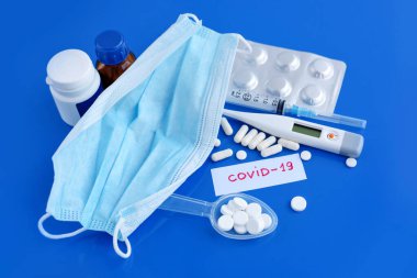 Tıbbi koruyucu maske, haplar, termometre, ilaçlar, şırıngalar mavi masada. Tehlikeli virüs COVID-19. Sağlık ve Tıp Konsepti.