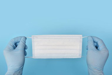 Mavi bir arka planda mavi lastik eldivenli tek kullanımlık tıbbi maske. Sağlık ve Koruma Konsepti.