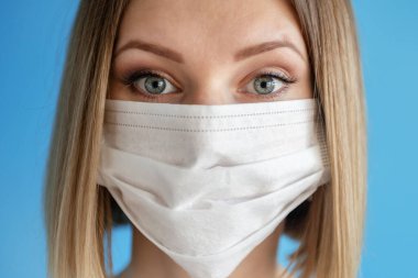 Yüz maskeli hemşire ya da doktor. Sağlık hizmeti, ameliyat. Mavi arka planda beyaz kadın modelinin yakın portresi.