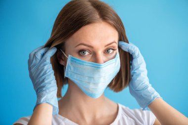 Yüz maskesi ve eldivenleri olan hemşire ya da doktor. Sağlık hizmeti, ameliyat. Mavi arka planda beyaz kadın modelinin yakın portresi.