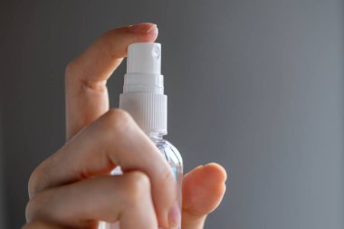 Kadın ya da kız, ellerinde dezenfekte edici sprey alkol ile ellerini dezenfekte ederek gri arka planda virüs bakterilerinin sağlığını önlemeye çalışıyor.