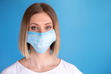 Yüz maskeli hemşire ya da doktor. Sağlık hizmeti, ameliyat. Mavi arka planda beyaz kadın modelinin yakın portresi.