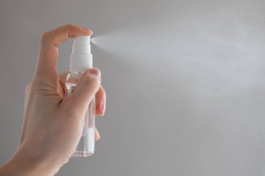 Kadın ya da kız, ellerinde dezenfekte edici sprey alkol ile ellerini dezenfekte ederek gri arka planda virüs bakterilerinin sağlığını önlemeye çalışıyor.